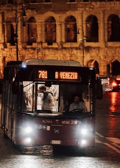 A bus driving down a Roman street night