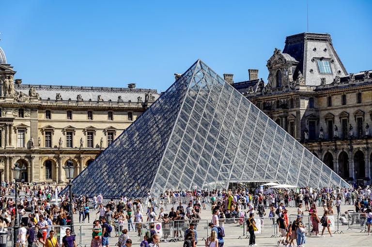 Crowded scene of the Louvre Pyramid in Paris, a famous historical landmark and tourist attraction.
